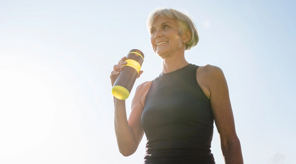 A woman in activewear smiling while holding a sports drink