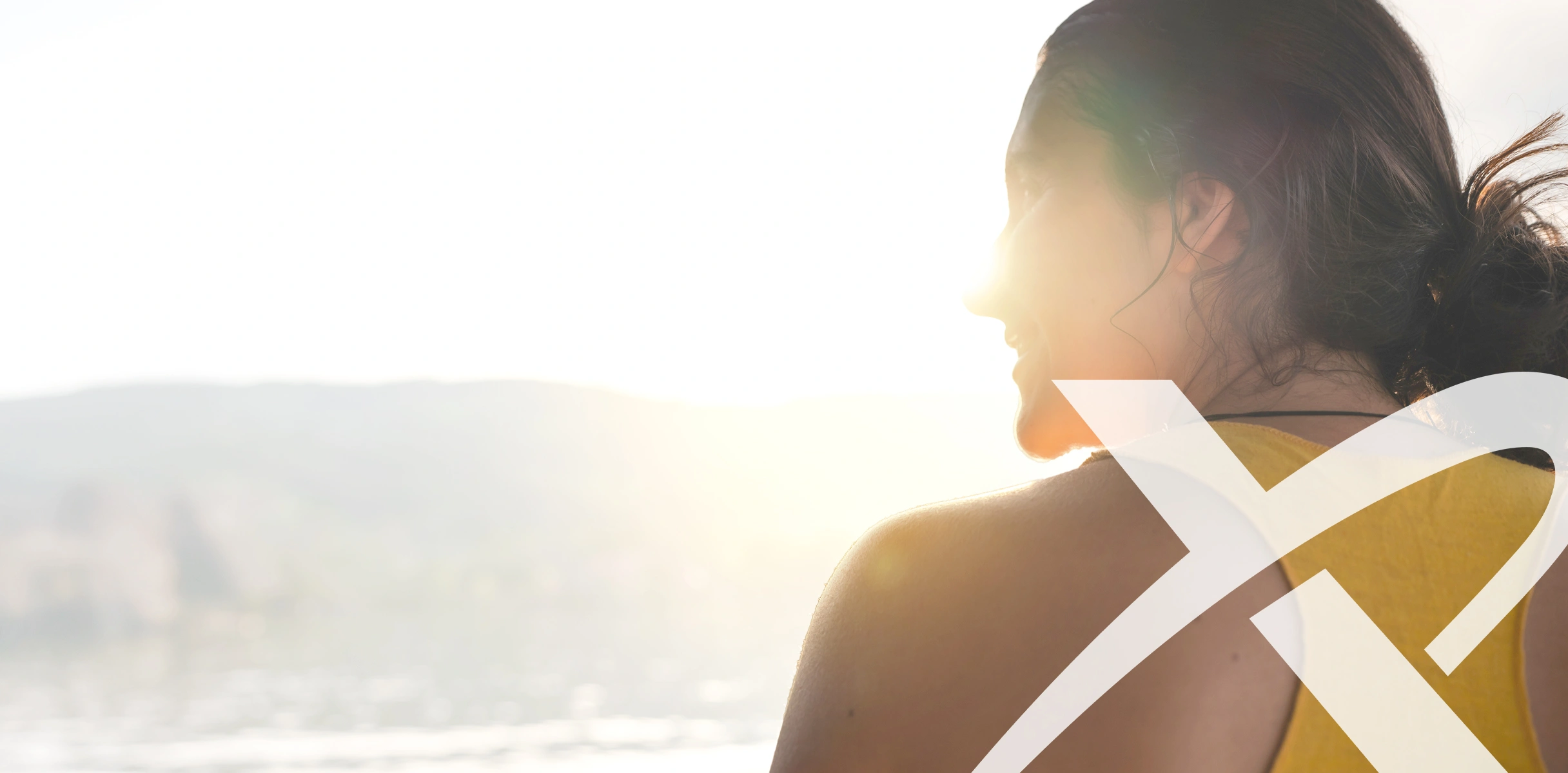 A woman smiling during sunset by the waterfront with the XYMOGEN logo juxtaposed on top