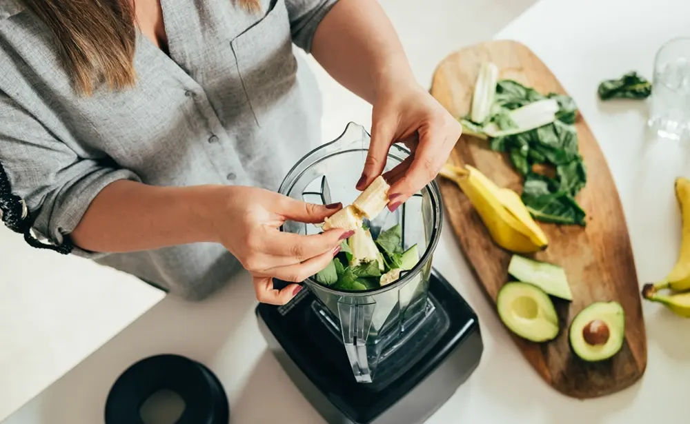 Woman putting vegetables on a blender.