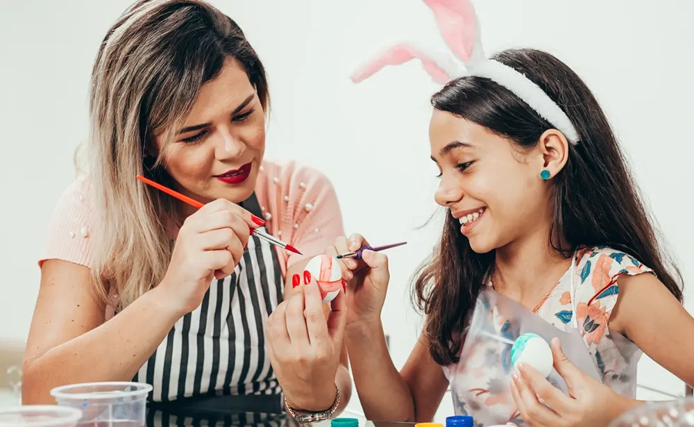 Woman and girl painting Easter eggs.